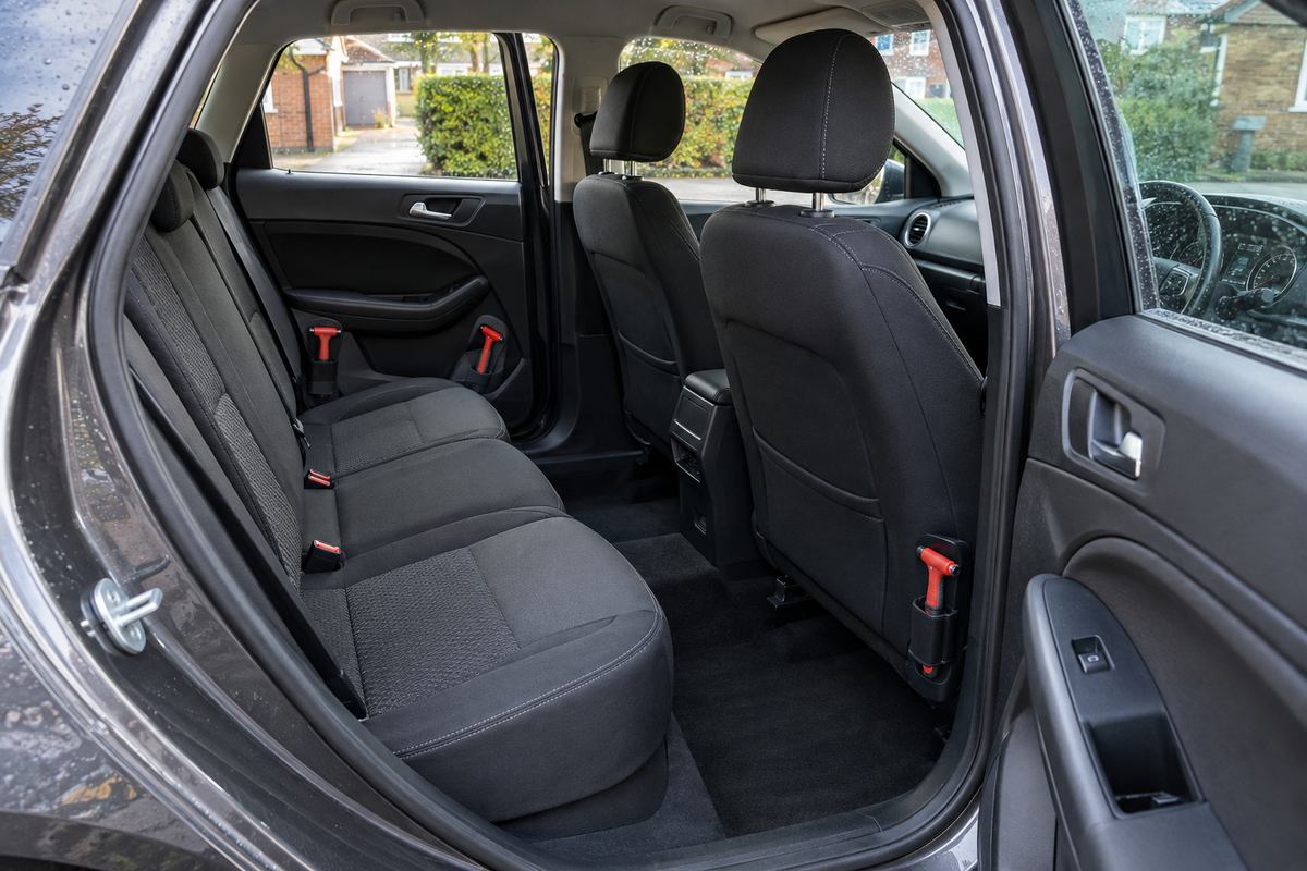 Three compact red emergency window breakers secured at separate reachable points inside a tidy unbranded right-hand-drive family car on a damp British driveway